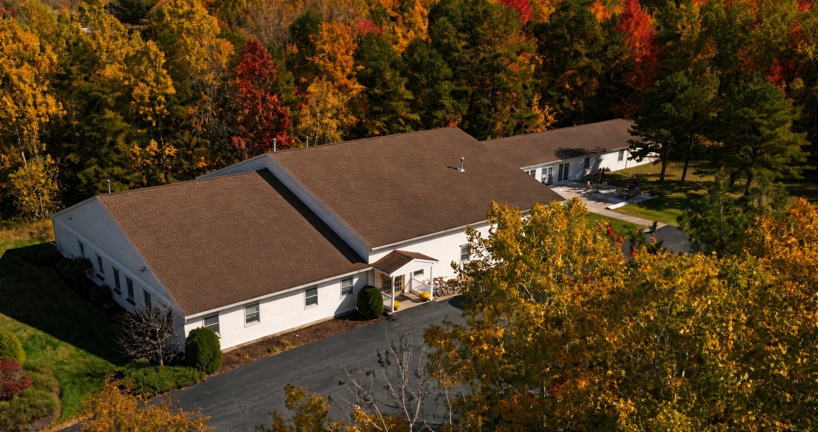 The Corrigan House from above, a long white building with a brown roof among autumn trees